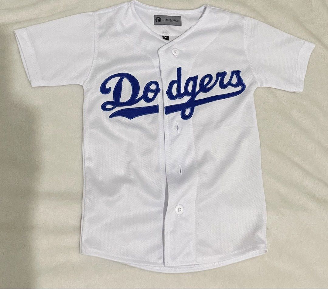 Los Angeles Dodgers White Baseball Jersey Size M (Category: Babies & Kids Fashion) located in Guiguinto. Submitted by beatan13 (Listing ID 1470320850, Image 1). Description: - Authentic Los Angeles Dodgers baseball jersey - Color: White with blue embroidered chest script - Style: Button-down front with short sleeves - Material: Lightweight, breathable athletic fabric - Size: Medium (tag at collar) - Condition: Great for streetwear, sports, and ca