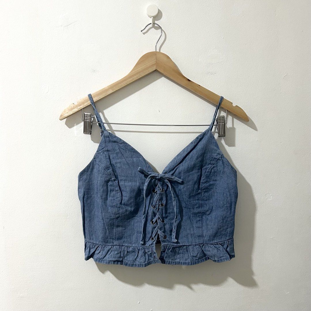[M] ACTIVE USA Chambray Front Tie Smocked Back Ruffled Hem Spaghetti Strap Crop Top (Category: Sleeveless) located in Tanza. Submitted by shop_qrated (Listing ID 1470245579, Image 2). Description: ACTIVE USA Chambray Front Tie Smocked Back Ruffled Hem Spaghetti Strap Crop Top. Medium on tag. Clean and ready to wear. This is a light blue denim or chambray spaghetti-strap crop top featuring a front lace-up closure with grommets, a V-neckline, adjus