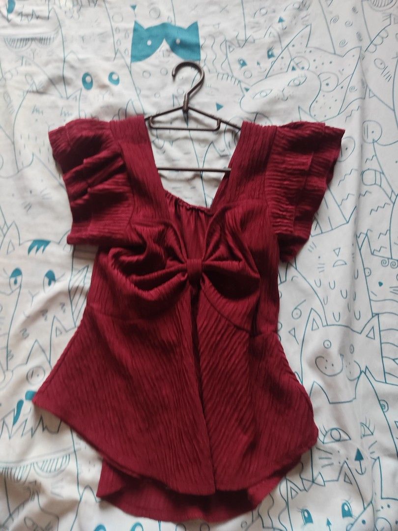 Maroon textured ruffle sleeve blouse with front bow detail (Category: Blouses) located in Caloocan City. Submitted by MovesLikeJeager (Listing ID 1470188558, Image 1). Description: - Color/Fabric: Deep maroon textured fabric, lightweight for warm weather - Design: Cute ruffle sleeves, front knotted bow detail at the chest - Fit: Flared hem style, flowy and comfortable - Styling: Pairs great with high-waisted jeans or a skirt - Condition: Wardrobe