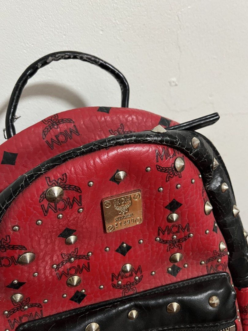 MCM Red Studded Leather Backpack (Category: Backpacks) located in Cabuyao City. Submitted by rdtrmt (Listing ID 1470151903, Image 3). Description: - Brand: MCM - Color: Bold red with black leather trim and silver-tone hardware - Design: Classic MCM monogram print covered in stylish metal studs - Features: Front zippered pocket with hardware pull, top grab handle, and signature front logo plaque - Straps: Adjustable black fabric shoulder straps fo