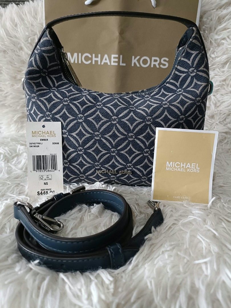 Michael Kors Ember Denim Jacquard Shoulder Bag (Category: Luxury Bags & Wallets) located in Iba. Submitted by royalgemini (Listing ID 1470172273, Image 1). Description: - Brand: Michael Kors Ember Handbag - Material: Blue denim monogram jacquard fabric with dark leather strap - Condition: Brand new with store tag (Original price: $448) - Hardware: Premium gold-tone lettering on the front - Closure: Secure zip-top closure - Inclusions: Detachable 