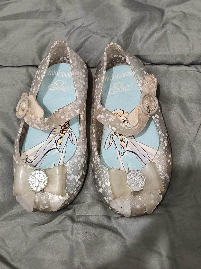 Mini Melissa Elsa Jelly Shoes (Category: Babies & Kids Fashion) located in Paranaque City. Submitted by abbethany1306 (Listing ID 1470331912, Image 1). Description: - Brand: Mini Melissa x Frozen (Elsa Collaboration) - Color/Finish: Glittery silver jelly flats - Details: Clear front bows with snowflake crystal accents - Closure: Adjustable buckle strap for a secure fit - Comfort: Signature sweet-scented Melflex plastic and Elsa-printed insoles - 