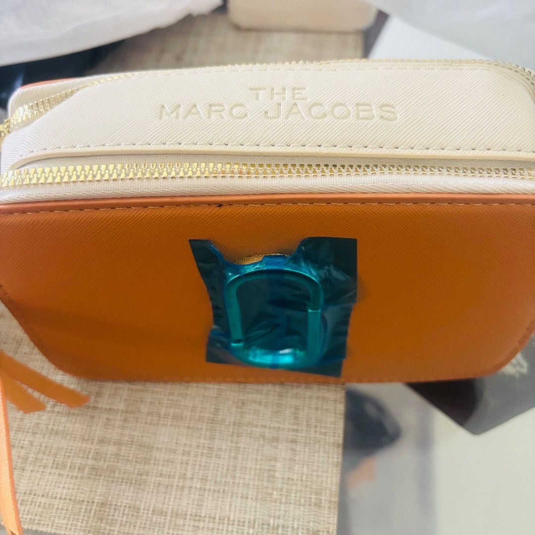 MJ The Snapshot Camera Bag (Category: Camera Bags & Carriers) located in Bulacan. Submitted by tytoluxe (Listing ID 1470206541, Image 3). Description: - Brand: MarcJacobs - Style: The Snapshot Camera Bag - Colorway: Striking Orange and White - Hardware: Gold-tone with iconic double J logo - Condition: Brand new (protective plastic still on front hardware) - Compartments: Double zip closure with top zip compartments - Strap: Includes fabric brande