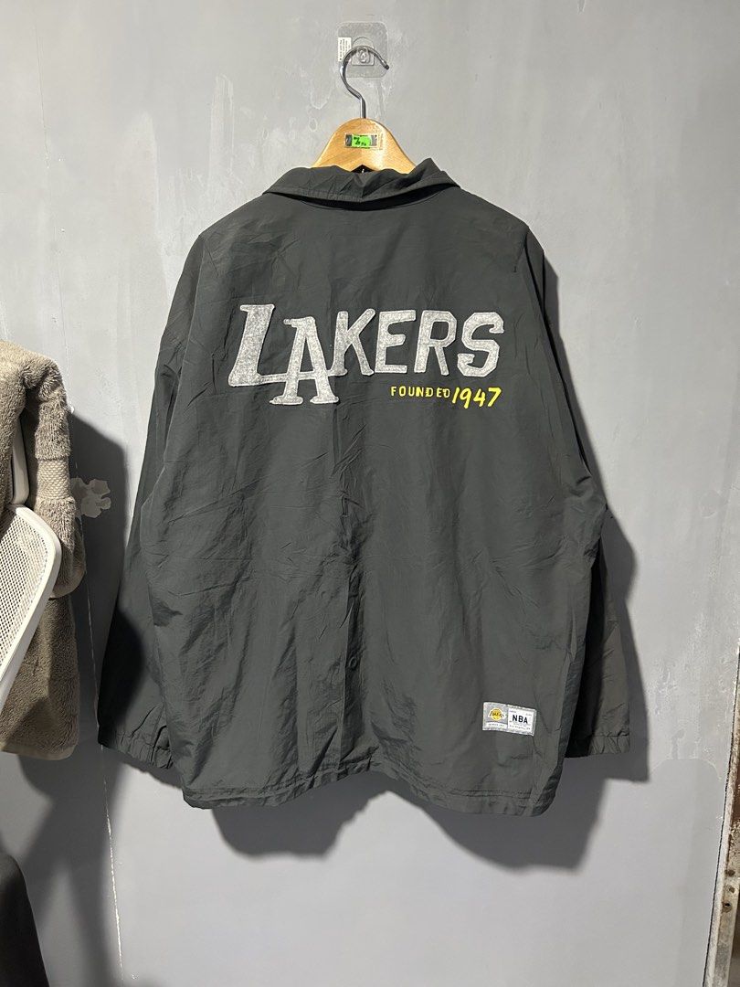 NBA Los Angeles Lakers Grey Coach Jacket (Category: Coats, Jackets and Outerwear) located in San Simon. Submitted by ericdeinla69664 (Listing ID 1470189274, Image 2). Description: - Official NBA Los Angeles Lakers merchandise - Color: Dark grey - Closure: Front snap buttons with collar neckline - Pockets: Convenient side pockets - Branding: Embroidered Lakers chest patch, large textured felt Lakers lettering with "Founded 1947" on the back, and N