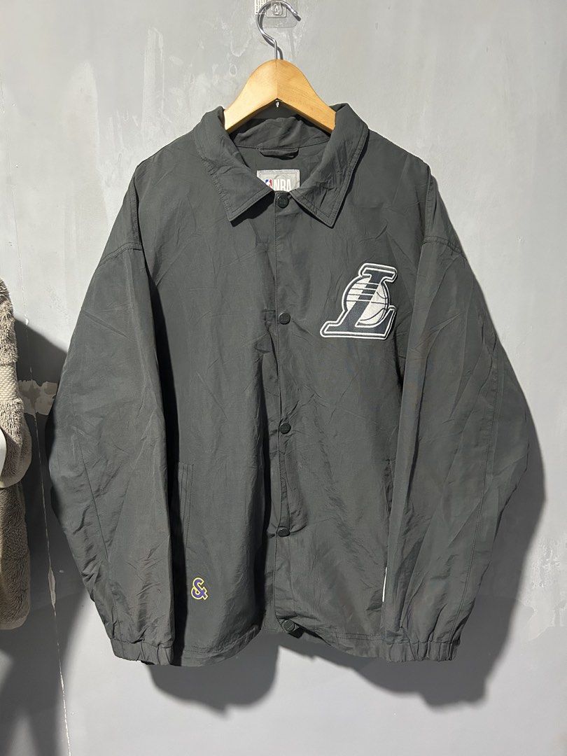 NBA Los Angeles Lakers Grey Coach Jacket (Category: Coats, Jackets and Outerwear) located in San Simon. Submitted by ericdeinla69664 (Listing ID 1470189274, Image 1). Description: - Official NBA Los Angeles Lakers merchandise - Color: Dark grey - Closure: Front snap buttons with collar neckline - Pockets: Convenient side pockets - Branding: Embroidered Lakers chest patch, large textured felt Lakers lettering with "Founded 1947" on the back, and N
