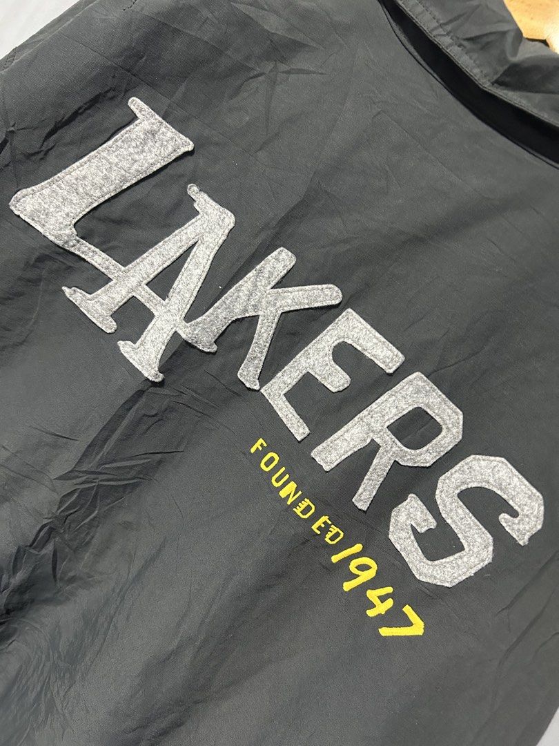 NBA Los Angeles Lakers Grey Coach Jacket (Category: Coats, Jackets and Outerwear) located in San Simon. Submitted by ericdeinla69664 (Listing ID 1470189274, Image 3). Description: - Official NBA Los Angeles Lakers merchandise - Color: Dark grey - Closure: Front snap buttons with collar neckline - Pockets: Convenient side pockets - Branding: Embroidered Lakers chest patch, large textured felt Lakers lettering with "Founded 1947" on the back, and N