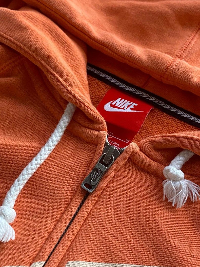 Nike Orange Zip-Up Hoodie (Category: Coats, Jackets and Outerwear) located in Manila. Submitted by raquimsyt (Listing ID 1470224771, Image 3). Description: - Brand: Nike - Style: Zip-up hoodie - Color: Bright orange with cream and navy front logo - Size: Medium (M) - Features: White drawstring hood with frayed tassel ends, front split kangaroo pocket, ribbed cuffs and hem - Condition: Pre-loved, well-maintained.