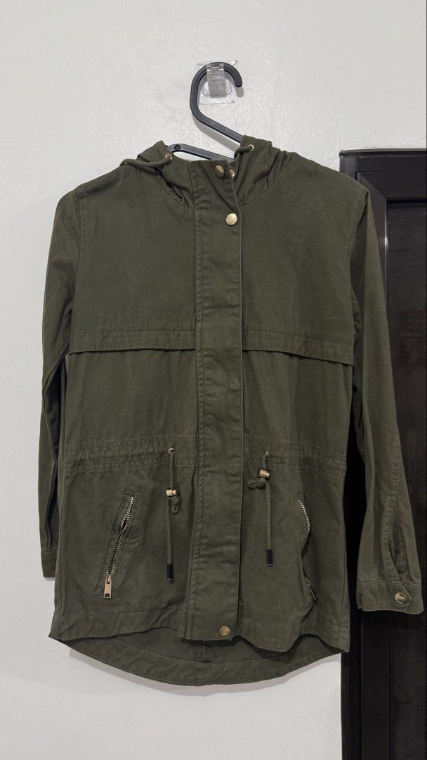 Olive green hooded utility jacket with gold hardware (Category: Coats, Jackets and Outerwear) located in Muntinlupa City. Submitted by maraaalpz (Listing ID 1470271889, Image 1). Description: - Color: Olive green - Style: Casual utility jacket with built-in hood - Fit: Adjustable drawstring waist for a customized fit - Pockets: Front zipper pockets - Closure: Snap button front with gold-toned buttons and zipper details - Details: Long sleeves wit