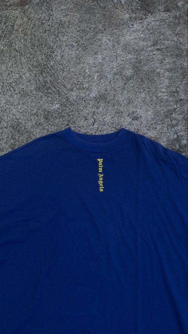 Palm Angels Blue Yellow Logo Tee (Category: Tshirts & Polo Shirts ) located in Iba. Submitted by gotmethrift (Listing ID 1470295193, Image 2). Description: - Brand: Palm Angels - Color: Royal blue with yellow gothic logos - Design: Small front neckline logo and giant vertical back logo - Fit: Oversized with drop shoulders and curved hem - Material: Heavyweight cotton - Style: Streetwear, pairs easily with jeans or cargos.