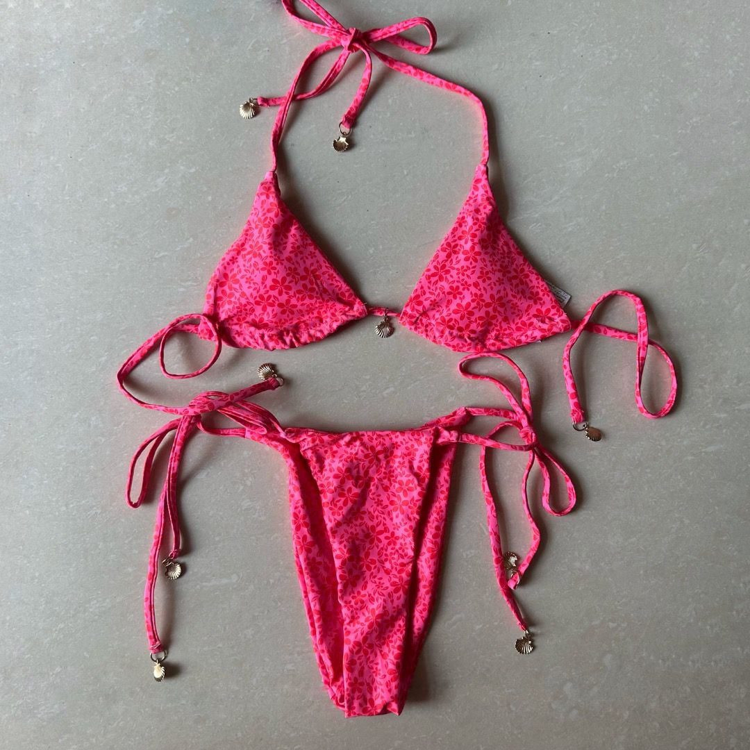 Pink Floral Bikini Set with Gold Shell Charms (Category: Bikinis & Swimsuits) located in Paranaque City. Submitted by yanie.ae (Listing ID 1470166460, Image 2). Description: - Style: Bright pink bikini set with small red floral pattern - Top: Triangle cut with adjustable string ties and gold-tone shell charms - Bottoms: Matching side-tie style with shell accents - Condition: Brand new / Unworn - Perfect for: Beach trips, vacations, and sunny days