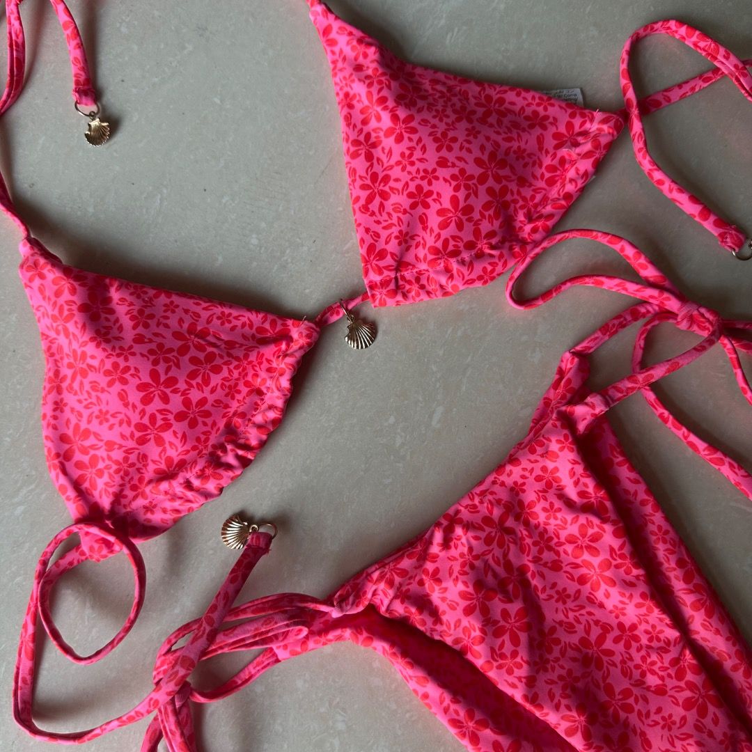 Pink Floral Bikini Set with Gold Shell Charms (Category: Bikinis & Swimsuits) located in Paranaque City. Submitted by yanie.ae (Listing ID 1470166460, Image 1). Description: - Style: Bright pink bikini set with small red floral pattern - Top: Triangle cut with adjustable string ties and gold-tone shell charms - Bottoms: Matching side-tie style with shell accents - Condition: Brand new / Unworn - Perfect for: Beach trips, vacations, and sunny days