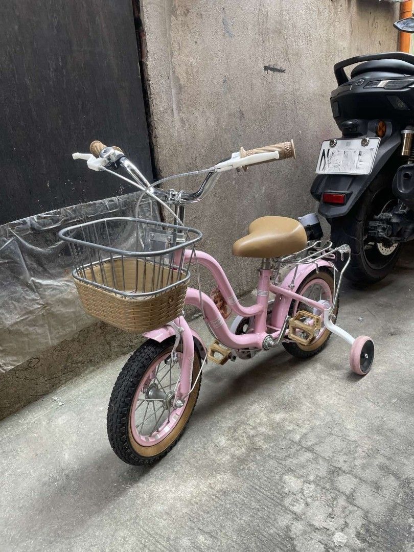 Pink Kids Bicycle with Training Wheels and Front Basket (Category: Bicycles) located in Caloocan City. Submitted by phil_thrifers (Listing ID 1470319321, Image 1). Description: - Color: Charming pink, perfect for young kids - Includes: Removable training wheels for beginners - Accessories: Front wire basket with woven base and a rear rack - Comfort & Style: Chrome handlebars with brown grips and a matching tan saddle seat - Safety: Pedals with bu