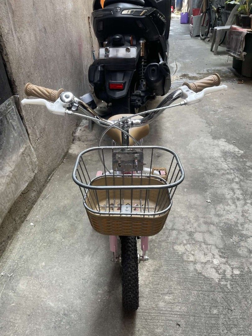 Pink Kids Bicycle with Training Wheels and Front Basket (Category: Bicycles) located in Caloocan City. Submitted by phil_thrifers (Listing ID 1470319321, Image 2). Description: - Color: Charming pink, perfect for young kids - Includes: Removable training wheels for beginners - Accessories: Front wire basket with woven base and a rear rack - Comfort & Style: Chrome handlebars with brown grips and a matching tan saddle seat - Safety: Pedals with bu