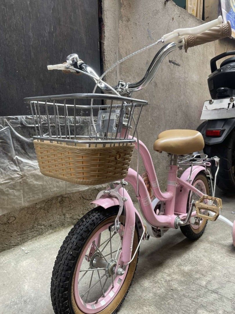 Pink Kids Bicycle with Training Wheels and Front Basket (Category: Bicycles) located in Caloocan City. Submitted by phil_thrifers (Listing ID 1470319321, Image 3). Description: - Color: Charming pink, perfect for young kids - Includes: Removable training wheels for beginners - Accessories: Front wire basket with woven base and a rear rack - Comfort & Style: Chrome handlebars with brown grips and a matching tan saddle seat - Safety: Pedals with bu