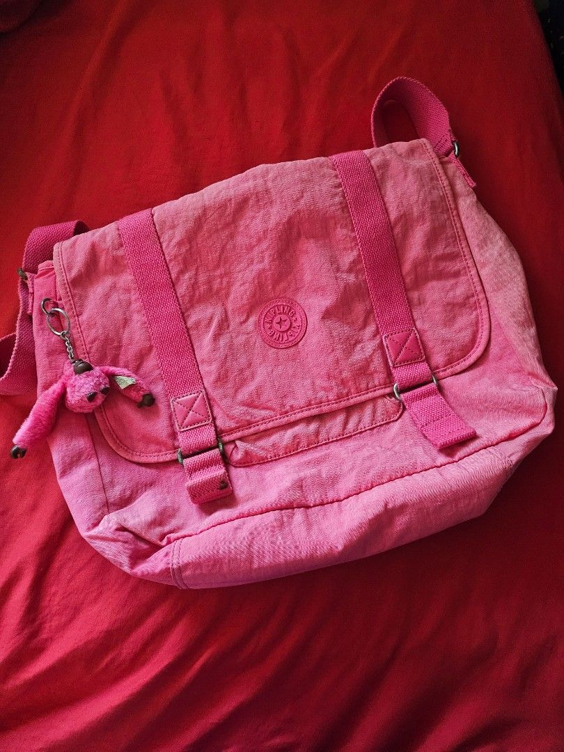 Pink Kipling Crossbody Bag with Monkey Keychain (Category: Cross-body Bags) located in Mandaluyong City. Submitted by ohwmaria (Listing ID 1470240841, Image 1). Description: - Needs washing, folds due to storage but they should smooth out naturally with use. Authentic Kipling messenger bag in a vibrant bright pink shade - Made from signature durable and lightweight crinkle nylon - Flap closure with double vertical straps and metal buckles - Conve