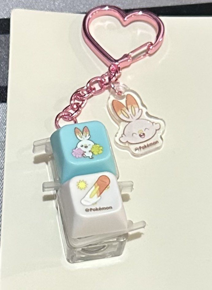 Pokepeace LED Keycap Bag charm (Category: Character Goods) located in Manila. Submitted by lunalux09 (Listing ID 1470159398, Image 1). Description: - Official Pokémon merchandise featuring Scorbunny - Includes a blue keycap and a white keycap with Scorbunny graphics - Comes with a dangling small acrylic Scorbunny charm and a pink heart clasp - Attached to a clear display holder - Perfect cute accessory for mechanical keyboard fans or bag decorati