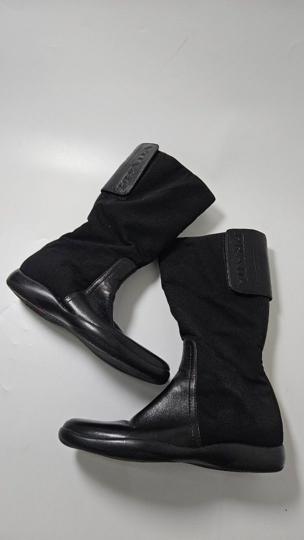 Prada Black Nylon and Leather Mid-Calf Boots (Category: Boots) located in Alfonso. Submitted by jbcamet (Listing ID 1470267296, Image 1). Description: - Brand: Prada - Style: Black mid-calf boots with a sporty design - Material: Combination of durable nylon fabric and premium leather - Closure: Back zipper with Prada Milano engraved hardware - Detailing: Leather top strap with embossed Prada logo and iconic red sole badge - Interior: Leather lini