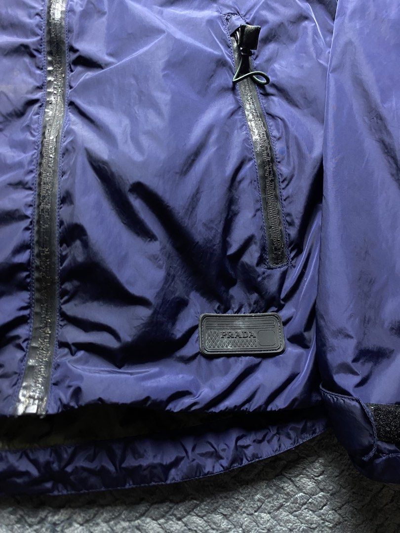 Prada Blue Nylon Hooded Jacket (Category: Coats, Jackets and Outerwear) located in Olongapo. Submitted by WAVYT (Listing ID 1470319567, Image 3). Description: - Prada hooded jacket in dark blue with an olive green inner lining - Crafted from water-resistant nylon fabric to keep you dry - Equipped with secure sealed zippers on the front and side pockets - Features the iconic rubber Prada patch logo near the bottom hem - Adjustable fit with Velcro 