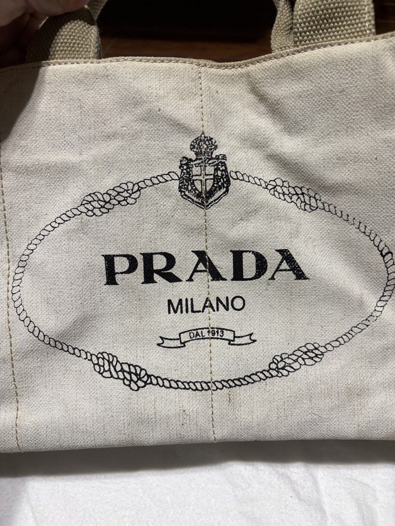 Prada Canapa Canvas Bag (Category: Luxury Bags & Wallets) located in Bulacan. Submitted by love2loved (Listing ID 1470281714, Image 3). Description: - Prada canvas tote bag - Features classic Prada logo on the front - Sturdy structured handles with gold-tone hardware - Secure top zip closure - Interior pockets for easy organization - Spacious interior fits all daily essentials - Condition: Shows minor wear and slight discoloration from normal use