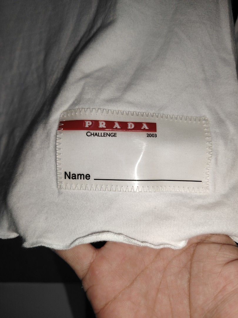 Prada Challenge 2003 White Long Sleeve Top (Category: Longsleeves) located in Roxas, Palawan. Submitted by act_thrift_palawan (Listing ID 1470286070, Image 3). Description: - Brand: Prada Challenge (2003 archive) - Color: White with red back stripe detail - Style: Long-sleeve top with scoop neckline - Details: Woven Prada patch at the lower front hem with name tag line, and Prada red neck branding - Fit/Sizing: Chest and waist measurements shown 