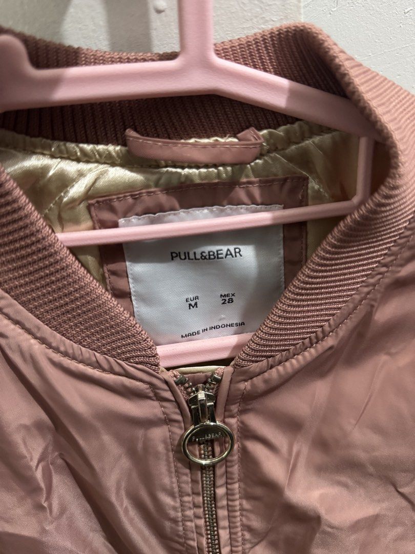 Pull&Bear Pink Bomber Jacket Size M (Category: Coats, Jackets and Outerwear) located in Manila. Submitted by nicefinds (Listing ID 1470286235, Image 2). Description: - Brand: Pull&Bear - Style: Lightweight bomber jacket - Color: Dusty pink with golden inner lining - Size: EUR M / MEX 28 - Closure: Front zipper with round ring pull - Pockets: Side pockets with snap buttons - Details: Ribbed collar, cuffs, and hem - Origin: Made in Indonesia.