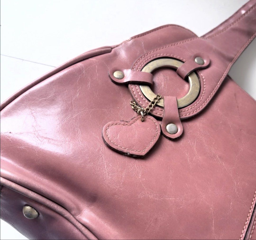 Rina Rich Pink Handbag Shoulder Bag (Category: Shoulder Bags) located in Calamba. Submitted by thethriftdame (Listing ID 1470244949, Image 2). Description: - Brand/Model: Rina Rich Handbag in Dusty Pink - Style: Trendy Y2K aesthetic with a structured design and center seam - Details: Chic circular metal ring accents and a matching heart charm on a chain - Interior: Fabric-lined with convenient zipper pockets - Protection: Fitted with bottom feet 