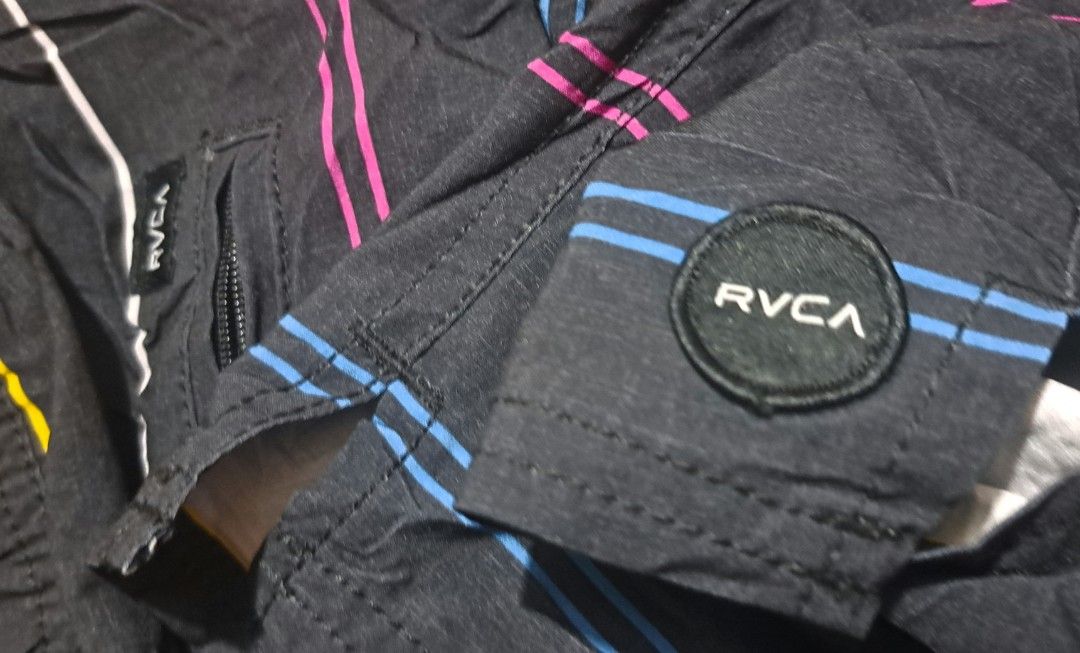 RVCA Striped Board Shorts Size M (Category: Swim Trunks & Board Shorts) located in San Fernando, Camarines Sur. Submitted by ladderaya (Listing ID 1470240840, Image 3). Description: - Brand: RVCA - Color: Black with colorful horizontal stripes - Size: Medium (fits waist 33-34 inches) - Material: 85% polyester, 15% elastane (stretch fabric) - Features: Blue drawstring waist, small side zipper pocket, and RVCA circle patch logo near the hem - Condi