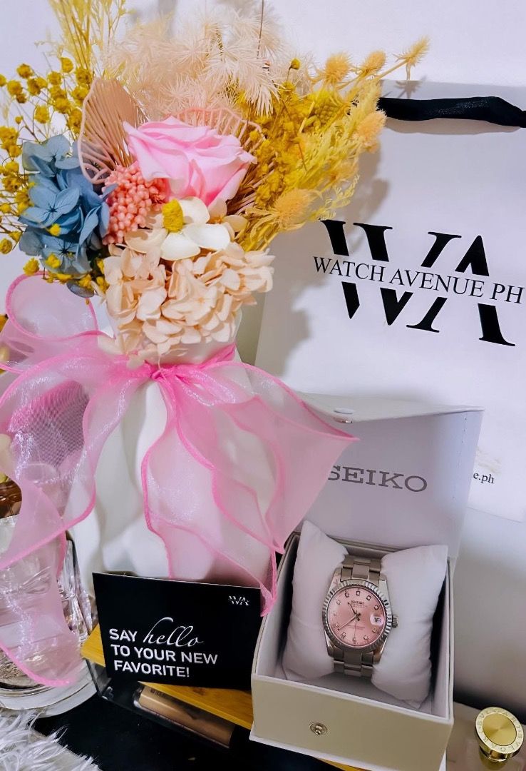 Seiko Watch Pink Dial Silver Tone (Category: Women's Watches) located in Caloocan City. Submitted by buritomma (Listing ID 1470157441, Image 1). Description: - Brand: Seiko - Dial: Soft pink with rhinestone hour markers and date window at 3 o'clock - Bezel: Elegant fluted design - Band: Silver-tone metal - Packaging: Original branded box with Watch Avenue PH paper bag and decorative flower setup - Condition: Brand new and ready for gifting.