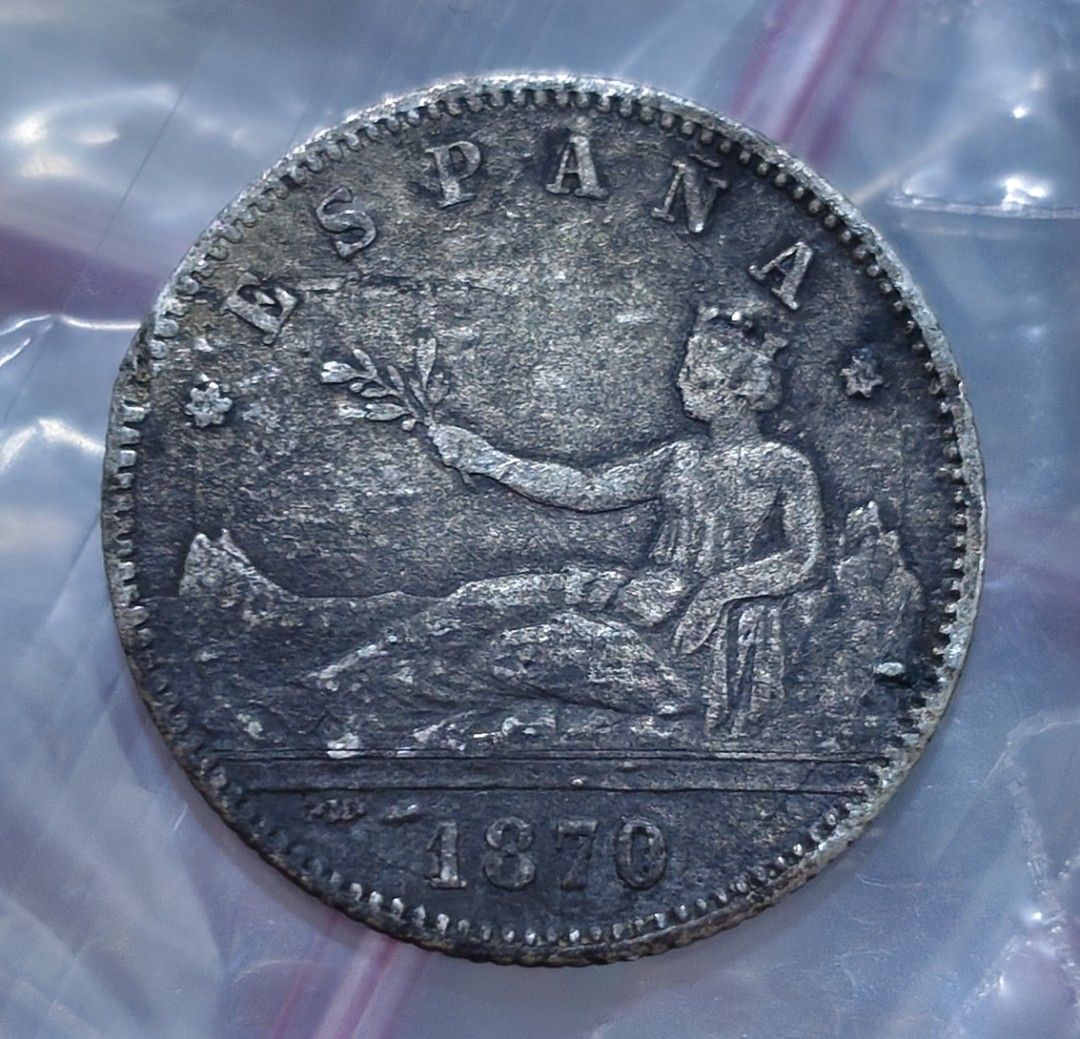 Spain 1870 1 Peseta Coin (Category: Currency) located in Taguig. Submitted by ezekiel103 (Listing ID 1470222167, Image 1). Description: - Item: 1870 Spanish 1 Peseta Coin - Obverse: Features the seated allegory of Hispania holding an olive branch with the date 1870 - Reverse: Displays the Spanish coat of arms flanked by pillars, with '200 PIEZAS EN KILOGRAMO' and 'UNA PESETA' - Condition: Heavy tarnish, natural toning, and surface wear consistent