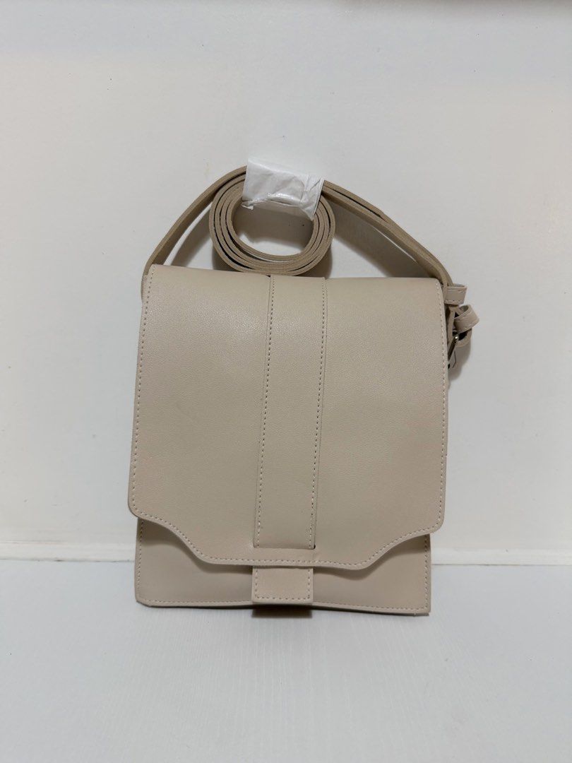 Straightforward structured crossbody sling bag (Category: Cross-body Bags) located in Makati City. Submitted by thrift.plethora (Listing ID 1470309753, Image 1). Description: - Color: Cream beige - Material: Premium faux leather - Design: Structured rectangular shape with a front flap closure and vertical accent panel - Strap: Adjustable strap with wrapped and secured top detail - Finish: Clean stitching throughout - Style: Versatile neutral tone