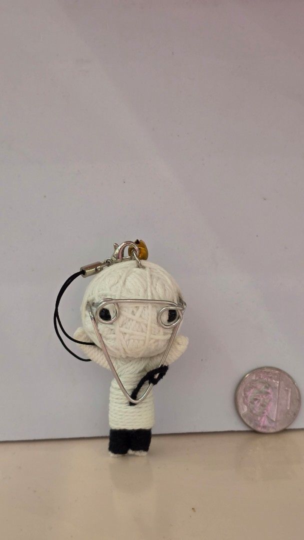 Voodoo Doll String Keychain with Bell and Glasses (Category: Character Goods) located in Imus. Submitted by a.niko (Listing ID 1470208342, Image 3). Description: - Handmade string voodoo doll keychain in white and black yarn - Features a mini metal pin attached to the head and body - Accented with a cute gold-toned bell on the strap loop - Comes with a phone strap, perfect for hanging on bags, keys, or phones - Unique and quirky accessory for dai