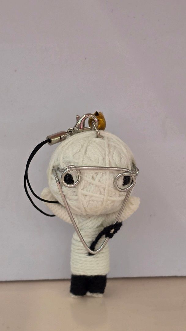 Voodoo Doll String Keychain with Bell and Glasses (Category: Character Goods) located in Imus. Submitted by a.niko (Listing ID 1470208342, Image 1). Description: - Handmade string voodoo doll keychain in white and black yarn - Features a mini metal pin attached to the head and body - Accented with a cute gold-toned bell on the strap loop - Comes with a phone strap, perfect for hanging on bags, keys, or phones - Unique and quirky accessory for dai