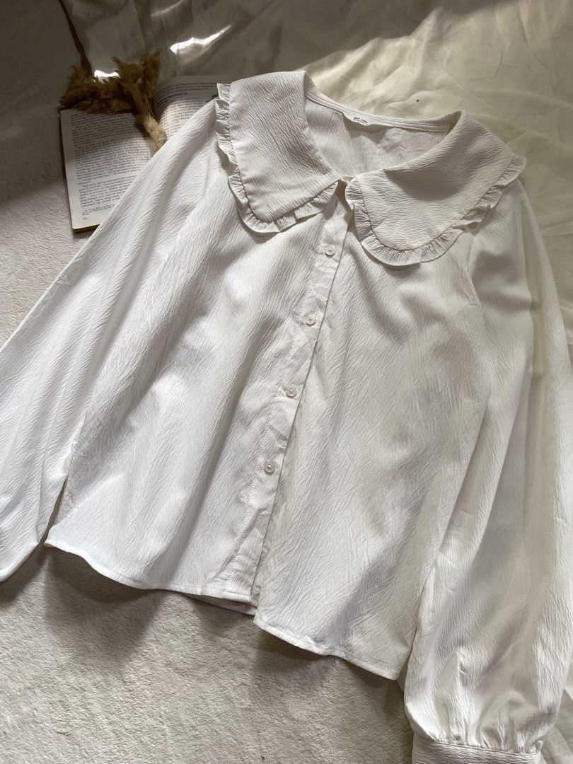 White Blouse with Ruffle Collar and Long Sleeves Medium 38 (Category: Blouses) located in Poro. Submitted by joyceyuu (Listing ID 1470185017, Image 2). Description: - Color: White - Style: Button-down blouse with a large rounded ruffle collar - Sleeves: Long balloon sleeves with fitted cuffs - Fabric: Light, textured material with subtle vertical patterns - Versatility: Classic piece that easily pairs with skirts or trousers - Occasion: Perfect f