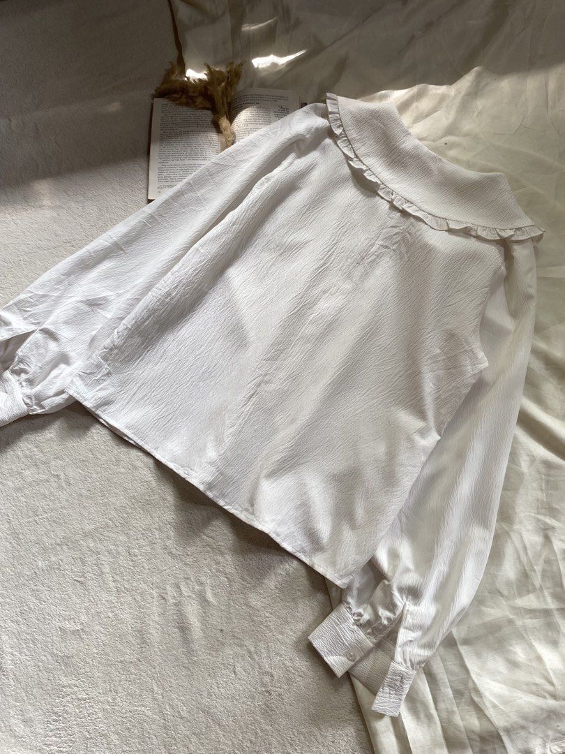 White Blouse with Ruffle Collar and Long Sleeves Medium 38 (Category: Blouses) located in Poro. Submitted by joyceyuu (Listing ID 1470185017, Image 3). Description: - Color: White - Style: Button-down blouse with a large rounded ruffle collar - Sleeves: Long balloon sleeves with fitted cuffs - Fabric: Light, textured material with subtle vertical patterns - Versatility: Classic piece that easily pairs with skirts or trousers - Occasion: Perfect f