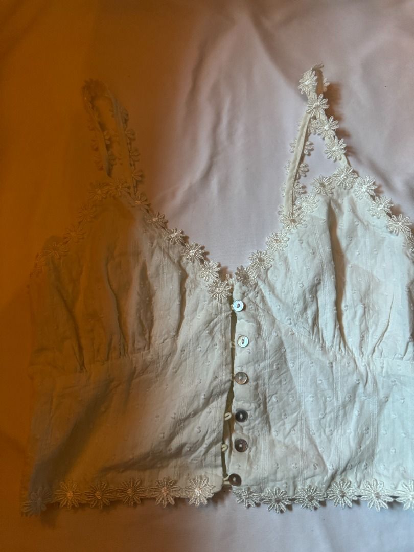 White Daisy Lace Trim Button Up Crop Top fits S-M (Category: Sleeveless) located in Cebu City. Submitted by _t.rix (Listing ID 1470179355, Image 1). Description: - Style: Sleeveless crop top in a sweet white textured dot fabric - Details: Delicate daisy lace trim on the neckline, straps, and hem with pearl-like front buttons - Fit: Smocked elastic band at the back for an easy and stretchy fit - Comfort: Made with soft and lightweight fabric, idea