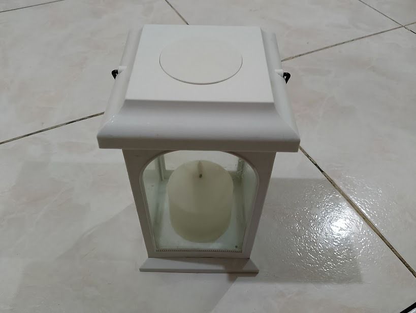 White decorative candle lantern with handle (Category: Lighting) located in Quezon City. Submitted by susmaryosep1 (Listing ID 1470260497, Image 1). Description: - Color: White with a black metal handle - Material: Metal frame with glass panes - Includes: Ivory pillar candle - Placement: Ideal for tabletops, shelves, or patios - Vibe: Adds simple, warm lighting to any room 500.