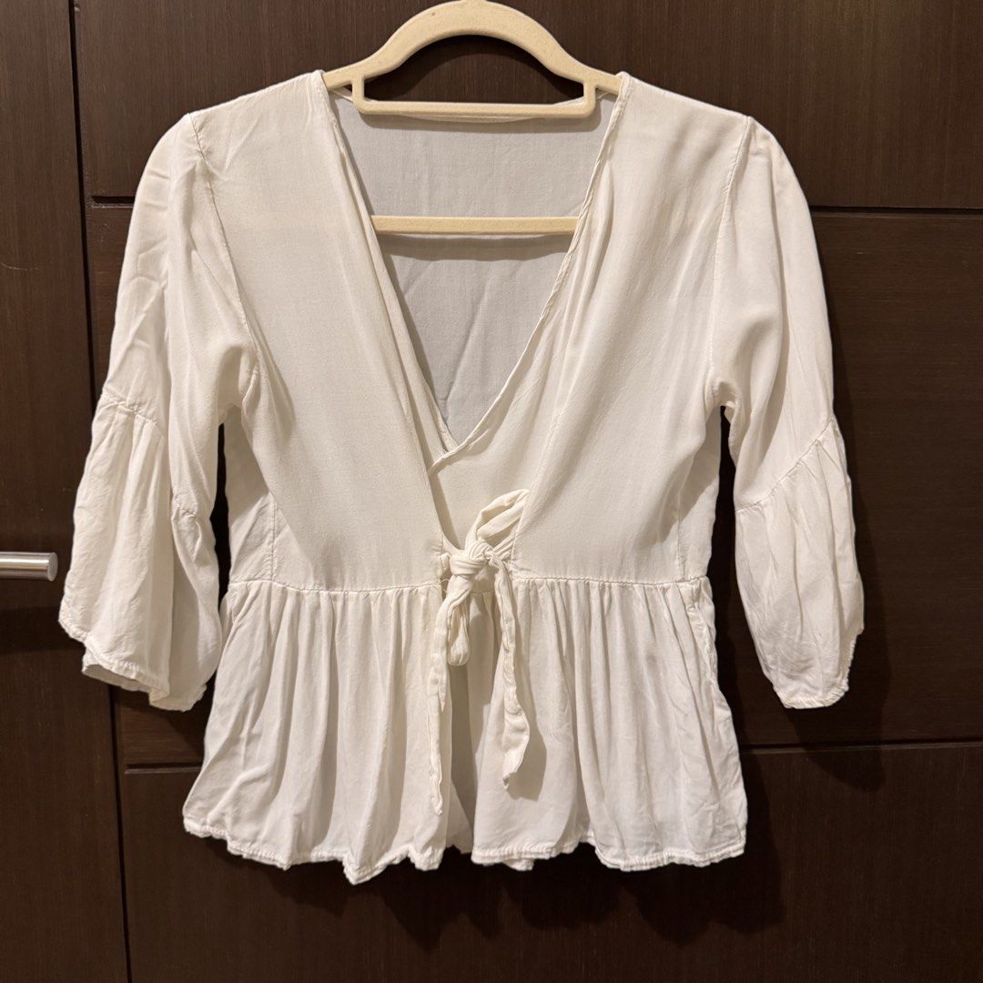 White Tie-Front Peplum Blouse with Flare Sleeves (Category: Blouses) located in Quezon City. Submitted by ianne.declutter (Listing ID 1470176413, Image 1). Description: - Color: White - Style: V-neck with tie-front closure and peplum waist - Sleeves: Three-quarter length with flared bell design - Fabric: Lightweight and breathable, ideal for warm weather - Versatility: Easy to pair with jeans or shorts for a casual look.