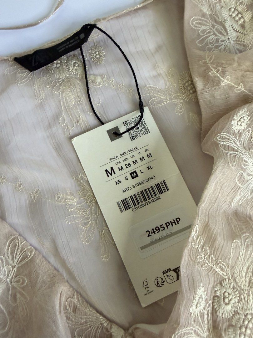 Zara Embroidered Ruffle Blouse Beige Size M (Category: Blouses) located in General Santos City (Dadiangas). Submitted by my_lzlove (Listing ID 1470241470, Image 2). Description: - Brand: Zara - Size: Medium (Brand new with original tags) - Original Price: ₱2,495 - Color: Beige with delicate white floral embroidery - Details: Deep V-neckline with ruffled trim, short flutter sleeves, and layered tiered ruffle hem - Fabric: Lightweight and textured 