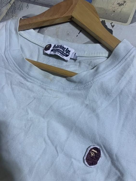 A Bathing Ape Bape White T-Shirt (Category: Tshirts & Polo Shirts ) located in San Jose del Monte. Submitted by dripfromthrift2 (Listing ID 1470483144, Image 2). Description: - Brand: A Bathing Ape (Bape) - Color: Light blue or white - Design: Embroidered small ape head patch on chest - Details: 'World Gone Mad' 1993-2093 neck tag and small ape logo tag on left cuff - Fit: Regular crew neck, short sleeves - Condition: Normal signs of wear.