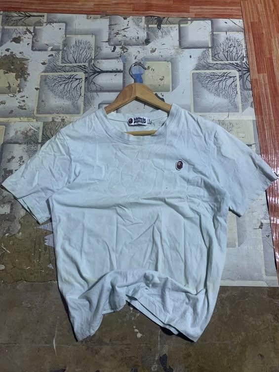A Bathing Ape Bape White T-Shirt (Category: Tshirts & Polo Shirts ) located in San Jose del Monte. Submitted by dripfromthrift2 (Listing ID 1470483144, Image 1). Description: - Brand: A Bathing Ape (Bape) - Color: Light blue or white - Design: Embroidered small ape head patch on chest - Details: 'World Gone Mad' 1993-2093 neck tag and small ape logo tag on left cuff - Fit: Regular crew neck, short sleeves - Condition: Normal signs of wear.