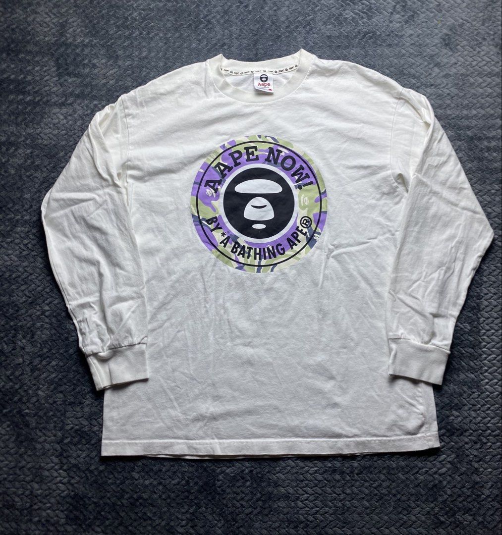 Aape By A Bathing Ape Long Sleeve Tee (Category: Tshirts & Polo Shirts ) located in Olongapo. Submitted by WAVYT (Listing ID 1470552412, Image 1). Description: White long sleeve shirt from Aape by A Bathing Ape. Big circular logo graphic on the chest with purple and green camo print inside. Classic Ape head right in the center. Neck tag inside and sleeve patch logo detail included. Size large printed on the inner collar label. Streetwear piece, c