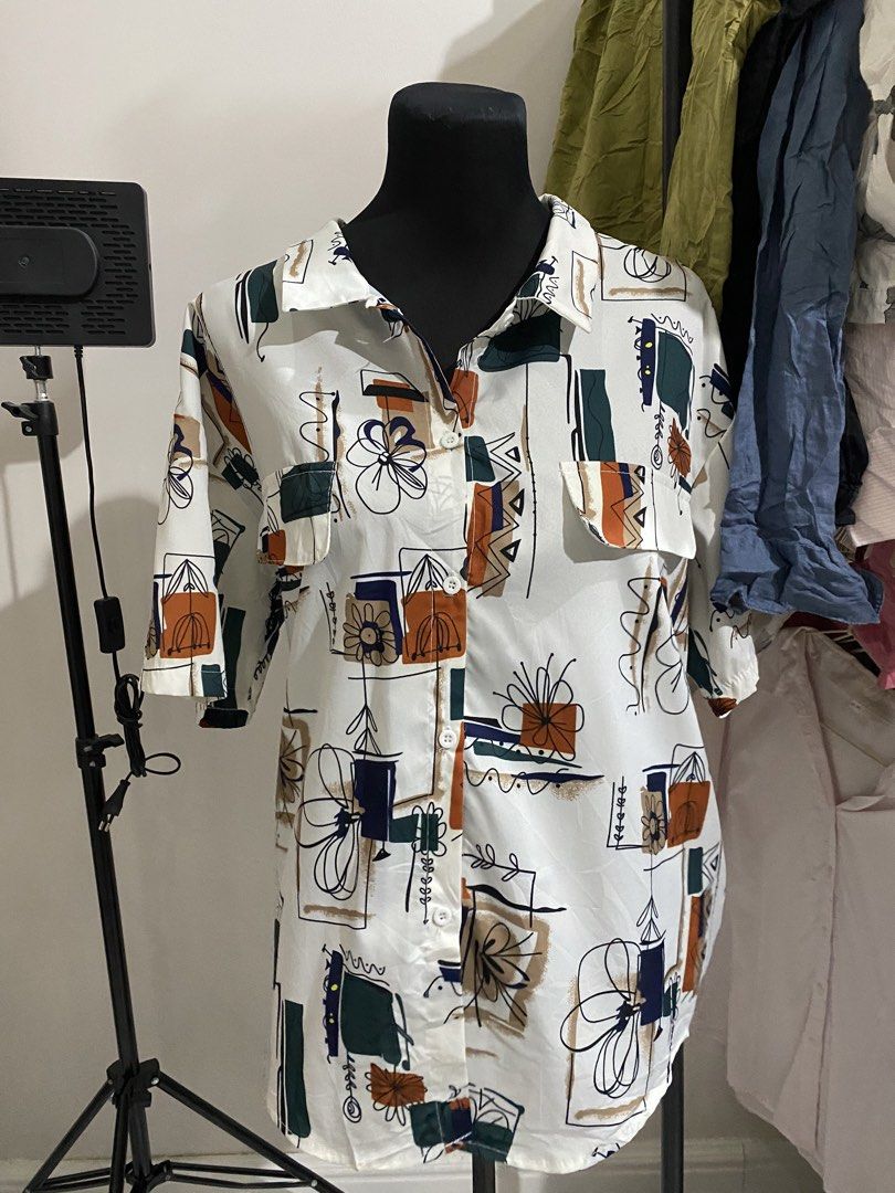 Abstract Art Print Button-Up Shirt (Category: Tshirts & Polo Shirts ) located in Manila. Submitted by mpt99876 (Listing ID 1470496986, Image 1). Description: - Style: Camp collar button-up shirt with abstract geometric and floral pattern - Colors: Dark green, orange, and blue - Fit: Relaxed fit with half-length sleeves - Features: Two front chest pockets with button flaps - Material: Lightweight and breathable fabric - Condition: Brand new / Exce