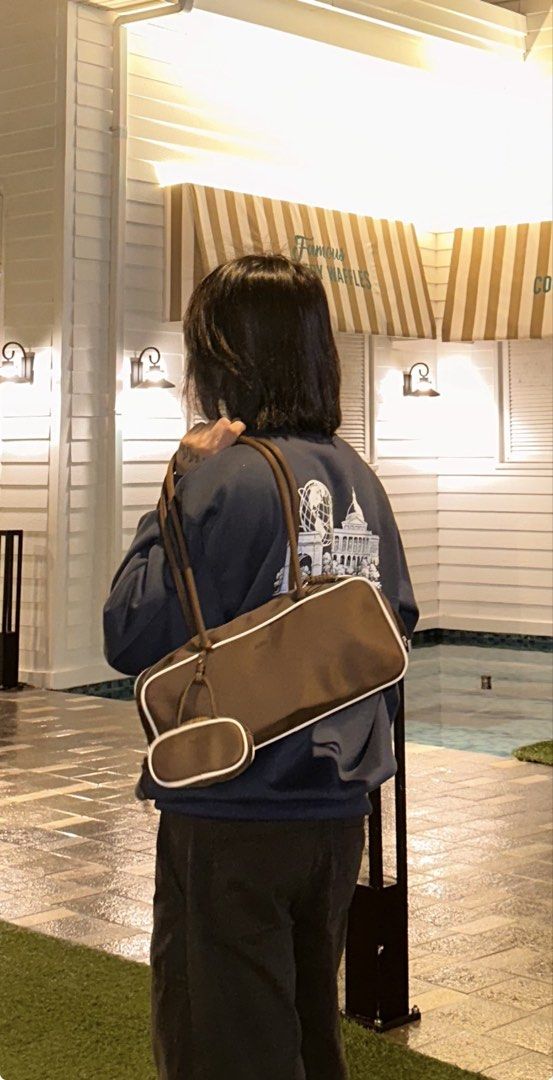 Alberto Bowler bag (brown) (Category: Shoulder Bags) located in Antipolo. Submitted by alparo1999 (Listing ID 1470378047, Image 2). Description: - Brand: Alberto - Material: Smooth, durable nylon-like fabric - Color: Brown with stylish white piping along the edges - Interior: Cream-colored lining featuring the brand's print - Closure: Secure top zipper - Bonus: Includes a matching mini pouch charm attached to the strap - Note: Side keychains show