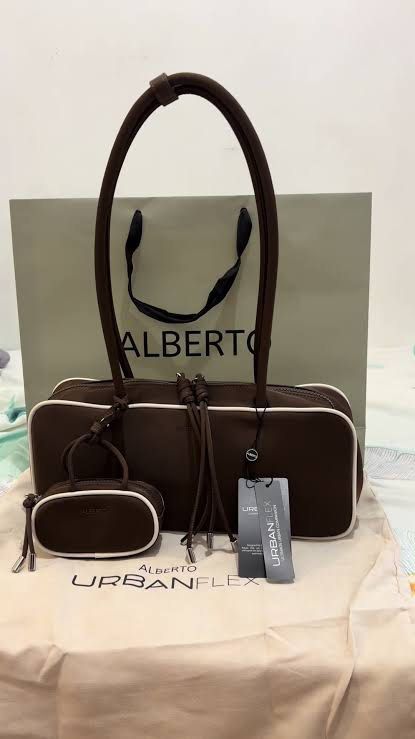 Alberto Bowler bag (brown) (Category: Shoulder Bags) located in Antipolo. Submitted by alparo1999 (Listing ID 1470378047, Image 1). Description: - Brand: Alberto - Material: Smooth, durable nylon-like fabric - Color: Brown with stylish white piping along the edges - Interior: Cream-colored lining featuring the brand's print - Closure: Secure top zipper - Bonus: Includes a matching mini pouch charm attached to the strap - Note: Side keychains show