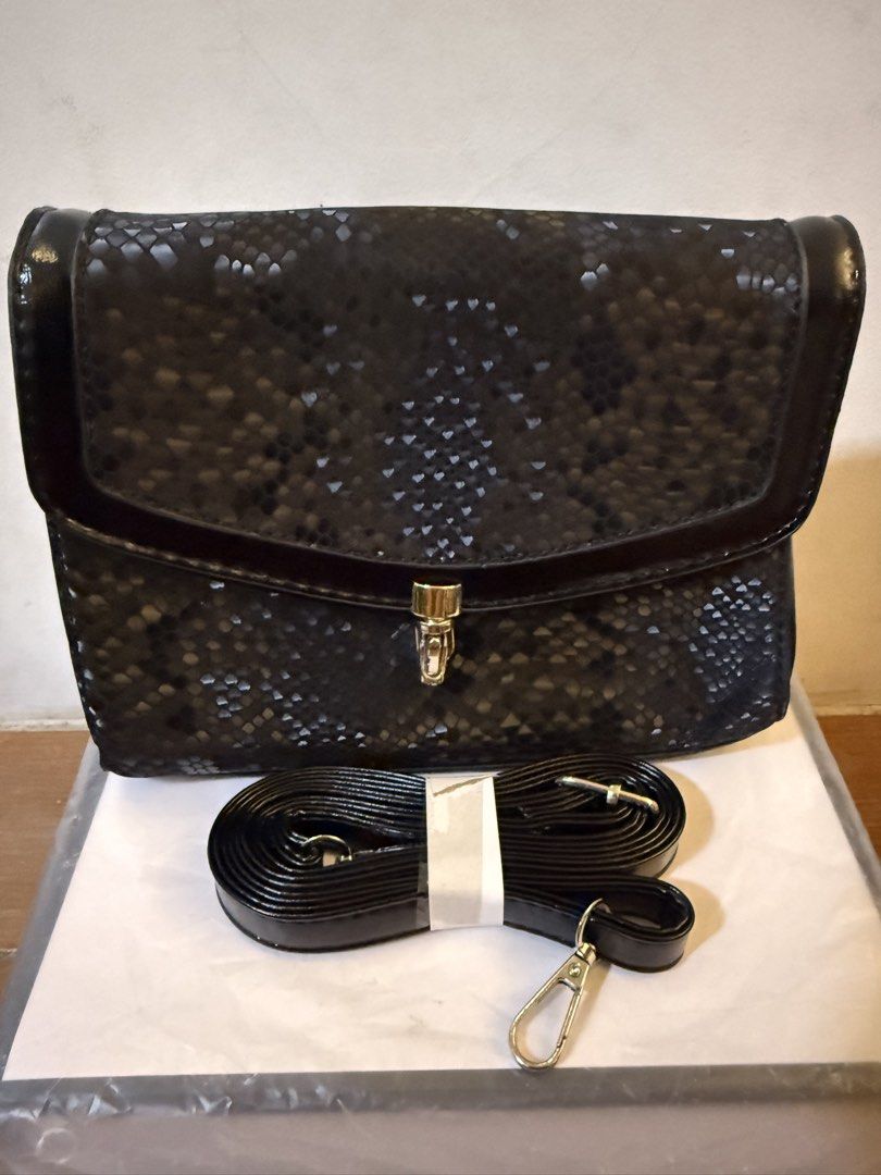 Black snakeskin pattern bag with strap (Category: Cross-body Bags) located in Bulacan. Submitted by emjay_17 (Listing ID 1470410672, Image 2). Description: - Condition: Brand new, never used and super clean inside - Design: Chic black snakeskin pattern with a secure flap closure and metal lock - Size: Compact dimensions, roughly 21cm across and 15cm tall - Interior: Stylish chevron-pattern fabric lining with a convenient middle zippered pocket - 