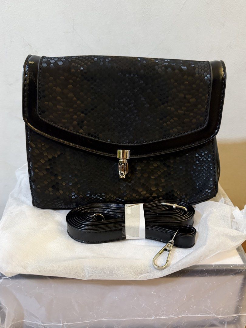 Black snakeskin pattern bag with strap (Category: Cross-body Bags) located in Bulacan. Submitted by emjay_17 (Listing ID 1470410672, Image 1). Description: - Condition: Brand new, never used and super clean inside - Design: Chic black snakeskin pattern with a secure flap closure and metal lock - Size: Compact dimensions, roughly 21cm across and 15cm tall - Interior: Stylish chevron-pattern fabric lining with a convenient middle zippered pocket - 
