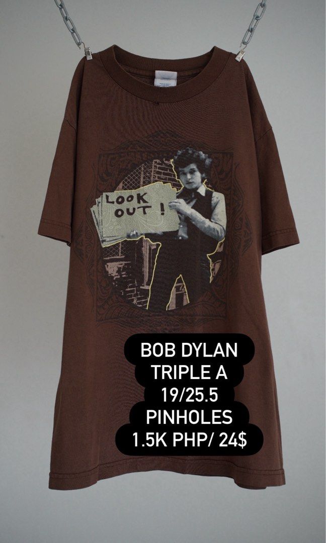 Bob Dylan Triple A Look Out Graphic Tee Brown (Category: Tshirts & Polo Shirts ) located in Muntinlupa City. Submitted by carl.samudio.carl.samudio56068 (Listing ID 1470492288, Image 1). Description: - Item: Vintage Bob Dylan graphic tee - Tag: Triple A - Color: Brown - Graphic: Young Bob Dylan holding a 'Look Out' sign - Size: 19" width x 25.5" length - Condition: Has minor pinholes on the fabric - Style: Classic rock merch.