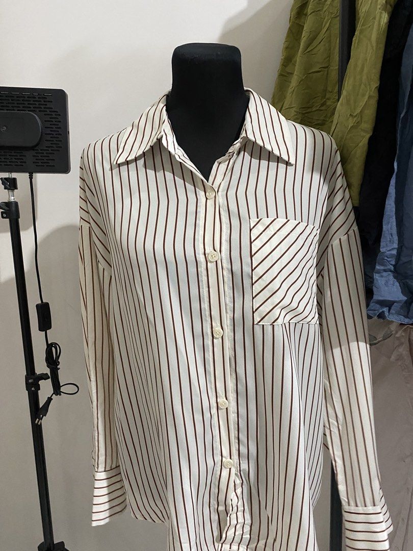 Brown Striped Button-Up Shirt Long Sleeve (Category: Longsleeves) located in Manila. Submitted by mpt99876 (Listing ID 1470496932, Image 3). Description: - Color/Pattern: White with brown vertical stripes - Pocket: Single chest pocket with ddiagonal stripe detail - Sleeves: Long sleeves with button cuffs - Fit: Relaxed, oversized fit - Fabric: Lightweight and breathable - Styling: Perfect to pair with jeans or trousers for a casual look.