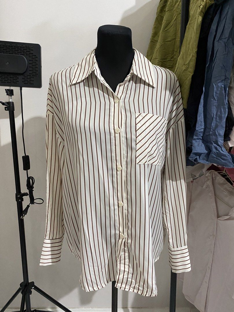 Brown Striped Button-Up Shirt Long Sleeve (Category: Longsleeves) located in Manila. Submitted by mpt99876 (Listing ID 1470496932, Image 1). Description: - Color/Pattern: White with brown vertical stripes - Pocket: Single chest pocket with ddiagonal stripe detail - Sleeves: Long sleeves with button cuffs - Fit: Relaxed, oversized fit - Fabric: Lightweight and breathable - Styling: Perfect to pair with jeans or trousers for a casual look.