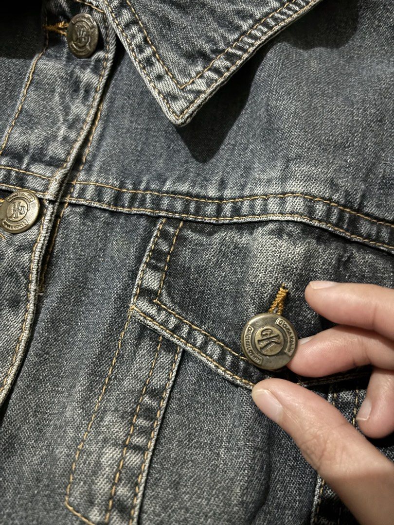 Calvin Klein dark grey denim jacket (Category: Coats, Jackets and Outerwear) located in Manila. Submitted by aysshxx (Listing ID 1470422371, Image 3). Description: - Brand: Calvin Klein - Color/Wash: Dark grey acid wash - Closure: Classic button-up front with branded metallic hardware - Pockets: Two chest pockets with button flaps - Details: Collar neckline and stylish contrast stitching throughout - Condition: Excellent / Ready to wear.